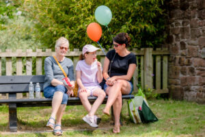 Three people sitting on a bench at the play park opening