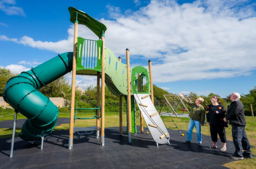 Three adults looking up at a piece of outdoor play equipment