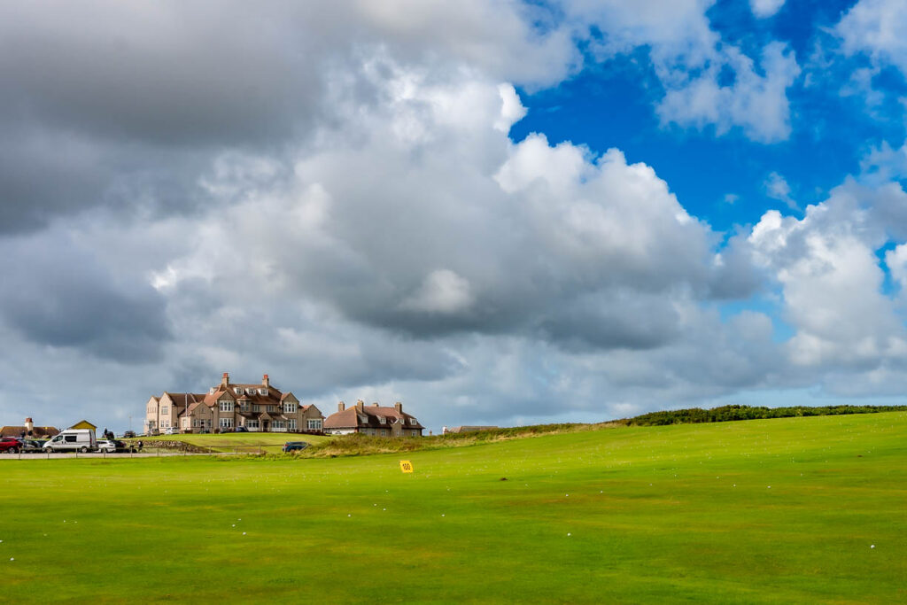 A building on a green golf course with blue sky and white clouds