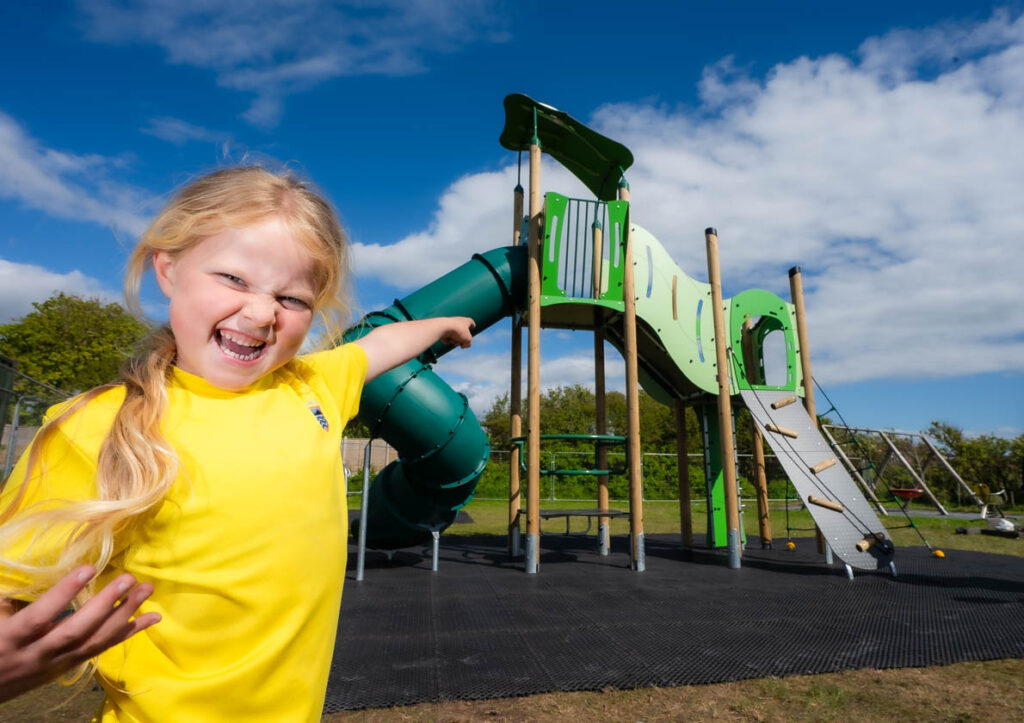 A young girl in yellow pointing to a piece of outdoor play equipment